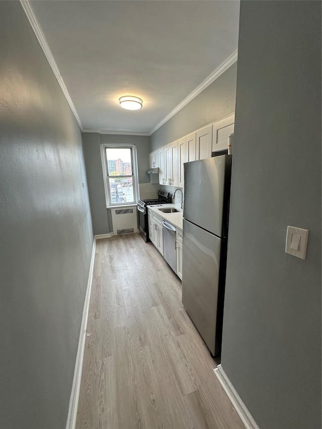 kitchen with sink, light hardwood / wood-style flooring, radiator heating unit, stainless steel appliances, and white cabinets