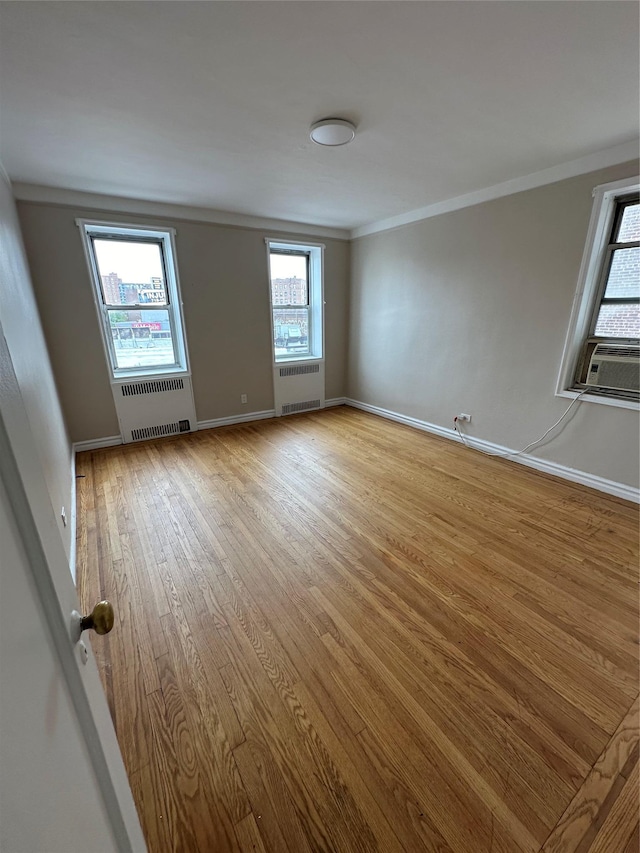 empty room with ornamental molding, radiator heating unit, and light wood-type flooring