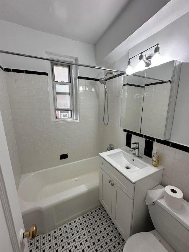 full bathroom with tile walls, tile patterned flooring, tiled shower / bath combo, vanity, and toilet