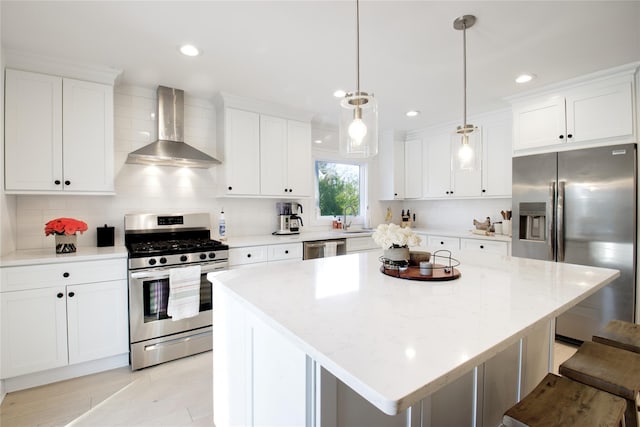 kitchen featuring wall chimney range hood, a breakfast bar area, hanging light fixtures, stainless steel appliances, and a center island