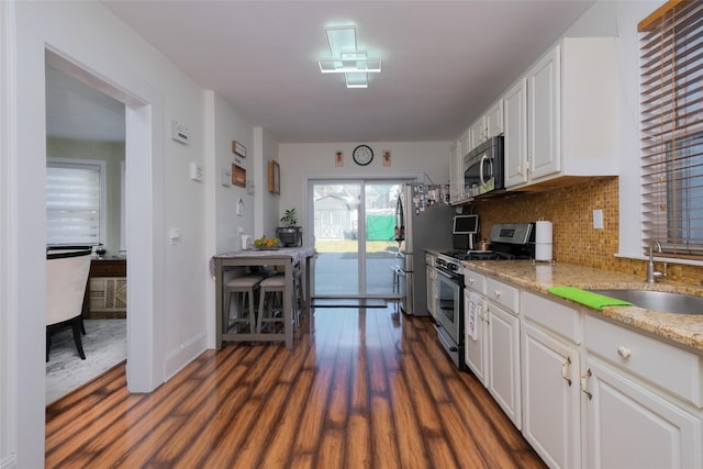 kitchen with sink, appliances with stainless steel finishes, white cabinetry, dark hardwood / wood-style floors, and decorative backsplash