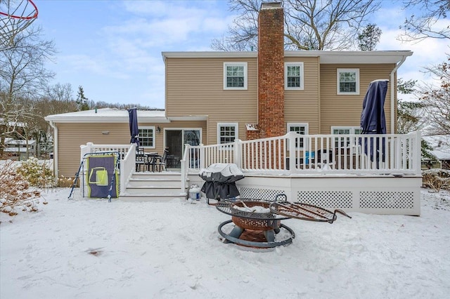 snow covered back of property with a deck and an outdoor fire pit