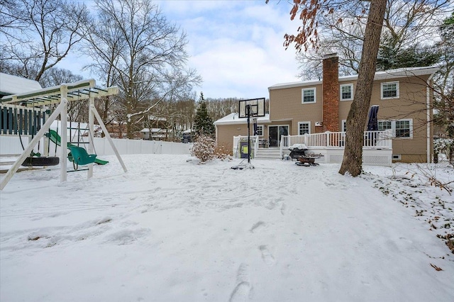 snowy yard with a playground and a deck