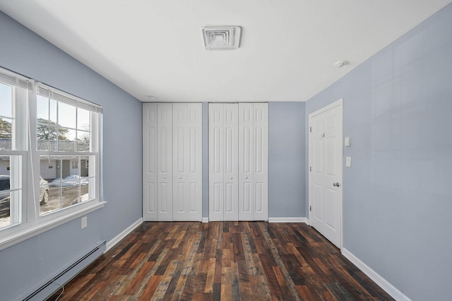 unfurnished bedroom with multiple closets, a baseboard heating unit, and dark hardwood / wood-style flooring