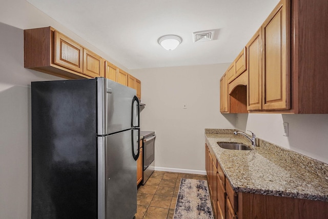 kitchen featuring appliances with stainless steel finishes, sink, dark tile patterned flooring, and light stone counters