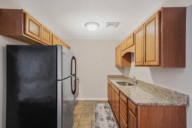 kitchen featuring stainless steel fridge, light stone countertops, sink, and light tile patterned floors