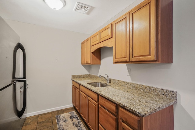 kitchen featuring fridge, sink, and light stone counters