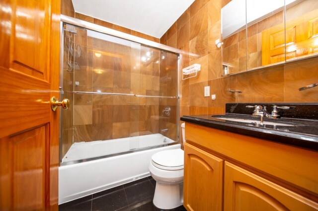 full bathroom featuring bath / shower combo with glass door, tile walls, vanity, toilet, and tile patterned floors