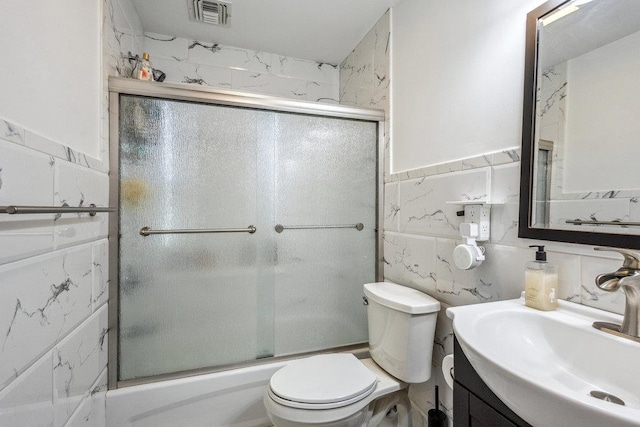 full bathroom featuring vanity, combined bath / shower with glass door, tile walls, and toilet