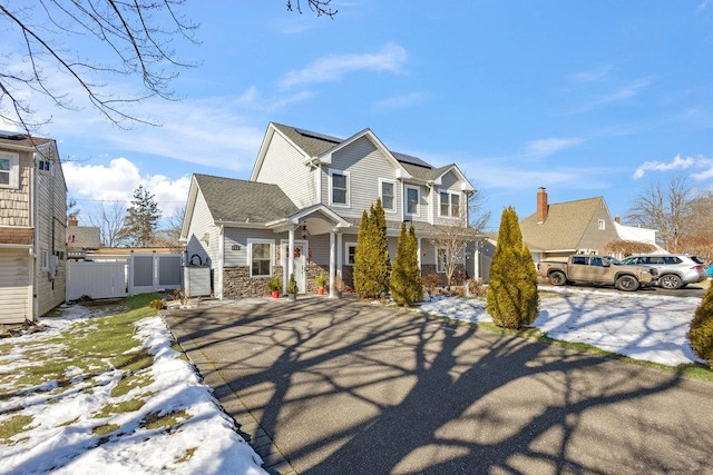 view of front of property with stone siding, fence, and roof mounted solar panels