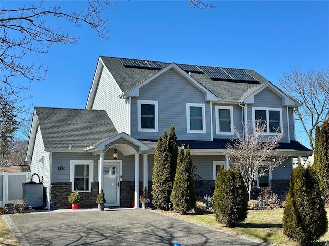 view of front of home featuring stone siding, roof mounted solar panels, and a shingled roof