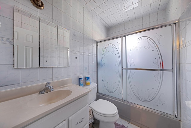 full bathroom featuring vanity, toilet, combined bath / shower with glass door, and tile walls