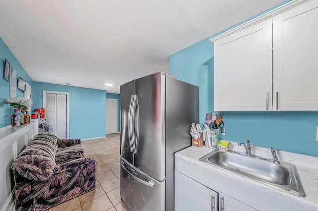 kitchen with white cabinetry, sink, light tile patterned floors, and stainless steel refrigerator