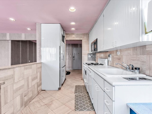 kitchen with white range with gas cooktop, sink, tile walls, and white cabinets