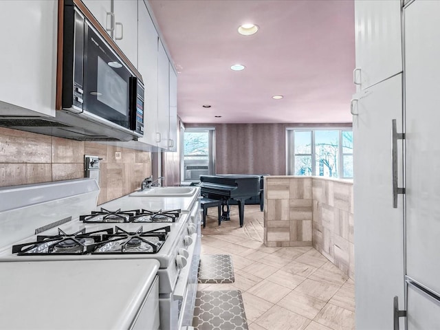 kitchen with a healthy amount of sunlight, white gas stove, tasteful backsplash, and white cabinets