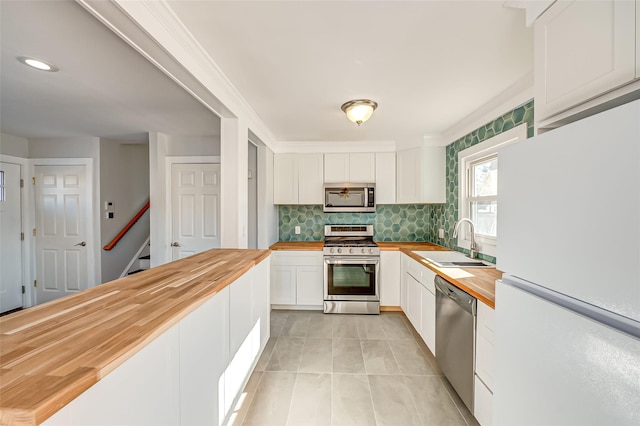 kitchen with butcher block countertops, sink, stainless steel appliances, white cabinets, and decorative backsplash