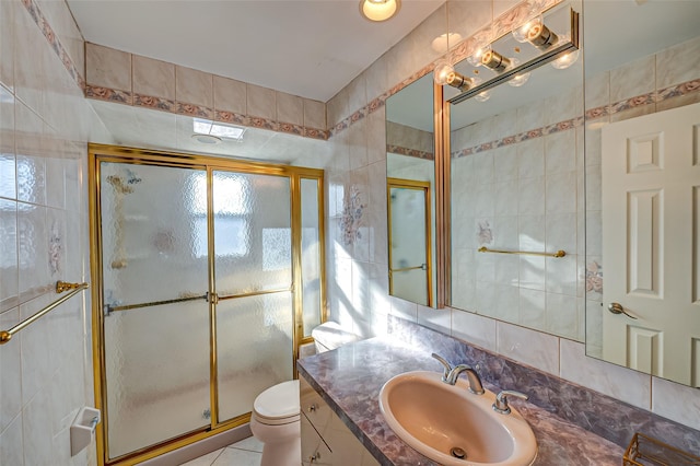 bathroom with tile patterned floors, toilet, tile walls, vanity, and a shower with door