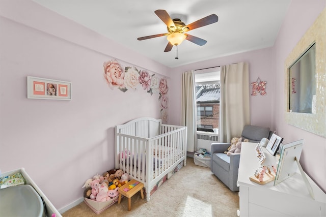 bedroom featuring ceiling fan, a crib, baseboards, and light colored carpet