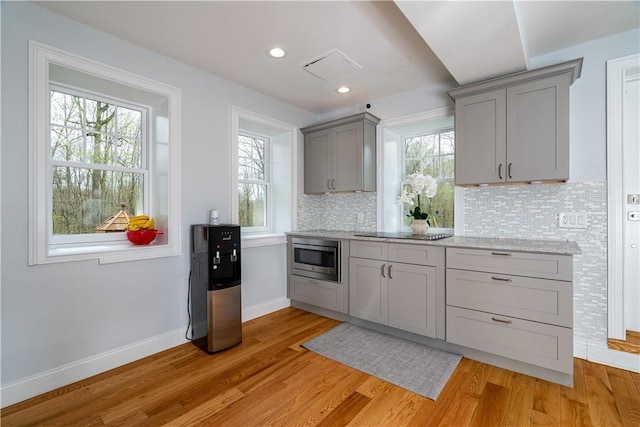 kitchen featuring tasteful backsplash, stainless steel microwave, gray cabinets, and light hardwood / wood-style flooring