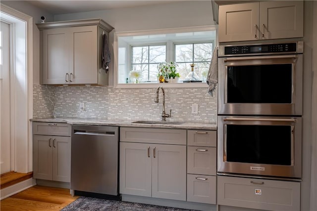 kitchen featuring tasteful backsplash, light stone countertops, appliances with stainless steel finishes, and sink