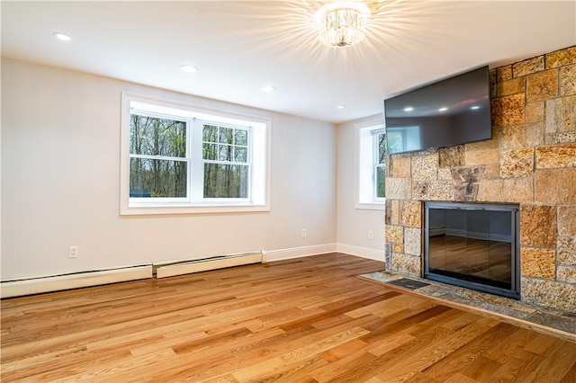 unfurnished living room with a stone fireplace, baseboard heating, and light wood-type flooring