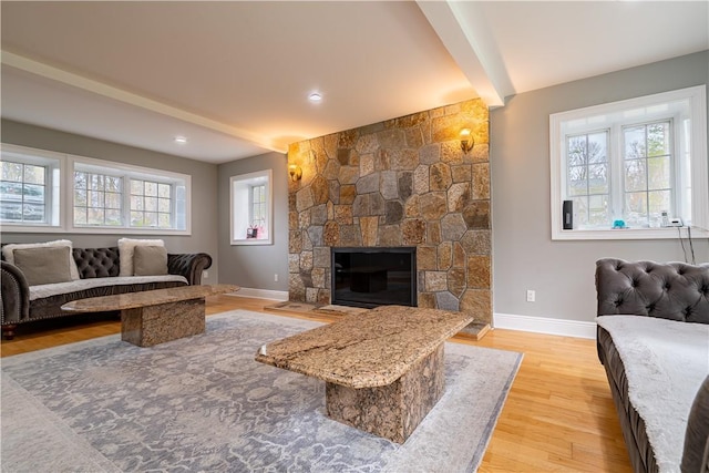 living room with beamed ceiling, a healthy amount of sunlight, a fireplace, and light hardwood / wood-style flooring