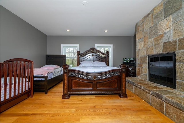 bedroom featuring a stone fireplace and light wood-type flooring