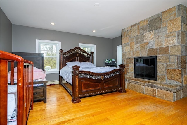 bedroom featuring wood-type flooring, a baseboard heating unit, and a fireplace