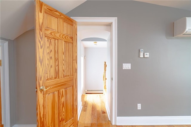 hall featuring lofted ceiling, a baseboard heating unit, a wall mounted AC, and light hardwood / wood-style floors