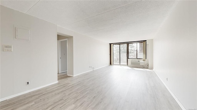 spare room featuring light hardwood / wood-style flooring, a wall of windows, a wall unit AC, and a textured ceiling