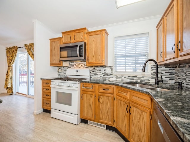 kitchen with a wealth of natural light, tasteful backsplash, sink, dark stone countertops, and stainless steel appliances