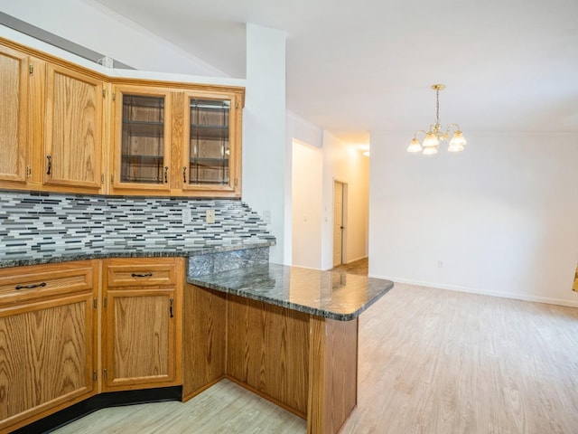 kitchen with decorative light fixtures, dark stone countertops, decorative backsplash, kitchen peninsula, and light hardwood / wood-style flooring