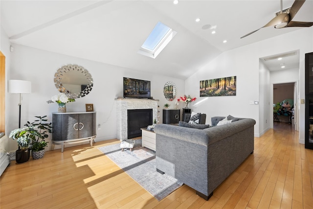 living room featuring wood-type flooring, a stone fireplace, and lofted ceiling with skylight