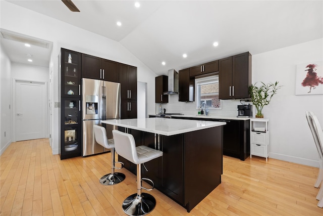 kitchen featuring tasteful backsplash, a breakfast bar area, a center island, stainless steel fridge with ice dispenser, and wall chimney range hood