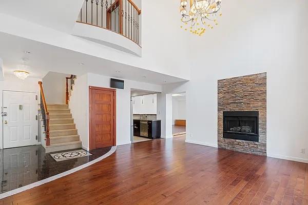 unfurnished living room featuring hardwood / wood-style flooring, a towering ceiling, a fireplace, and a chandelier