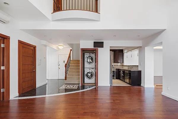 unfurnished living room featuring sink, wood-type flooring, a wall unit AC, stacked washing maching and dryer, and a high ceiling