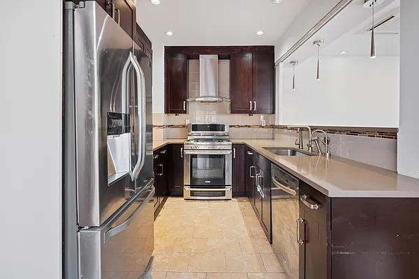 kitchen featuring stainless steel appliances, dark brown cabinets, sink, and wall chimney range hood