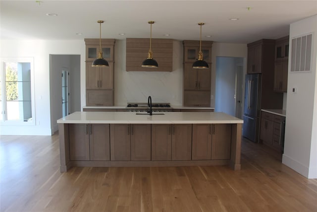 kitchen featuring high end fridge, light wood-type flooring, hanging light fixtures, and a large island with sink