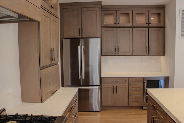 kitchen featuring stainless steel refrigerator, tasteful backsplash, beverage cooler, light stone countertops, and light hardwood / wood-style flooring