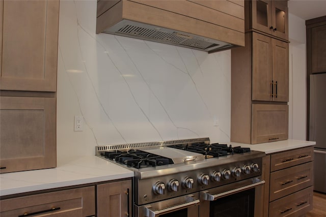 kitchen featuring light stone counters, fridge, custom range hood, and range with two ovens