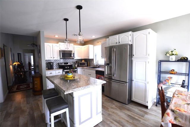 kitchen featuring stainless steel appliances, a kitchen island, white cabinets, and decorative light fixtures