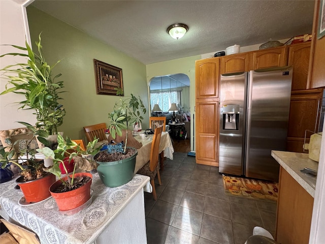 kitchen featuring brown cabinets, dark tile patterned flooring, a textured ceiling, stainless steel fridge with ice dispenser, and light countertops