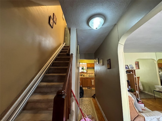 staircase featuring arched walkways, a textured ceiling, baseboards, and wood finished floors