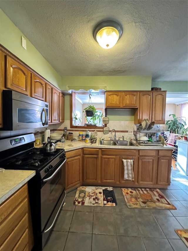 kitchen with stainless steel microwave, range with gas cooktop, light countertops, brown cabinets, and a sink