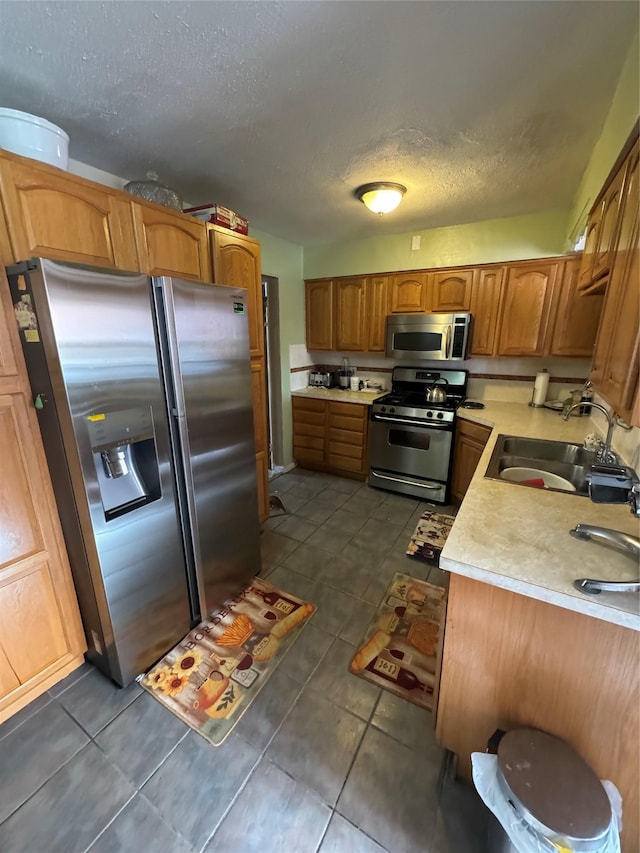 kitchen with dark tile patterned floors, light countertops, brown cabinets, stainless steel appliances, and a sink