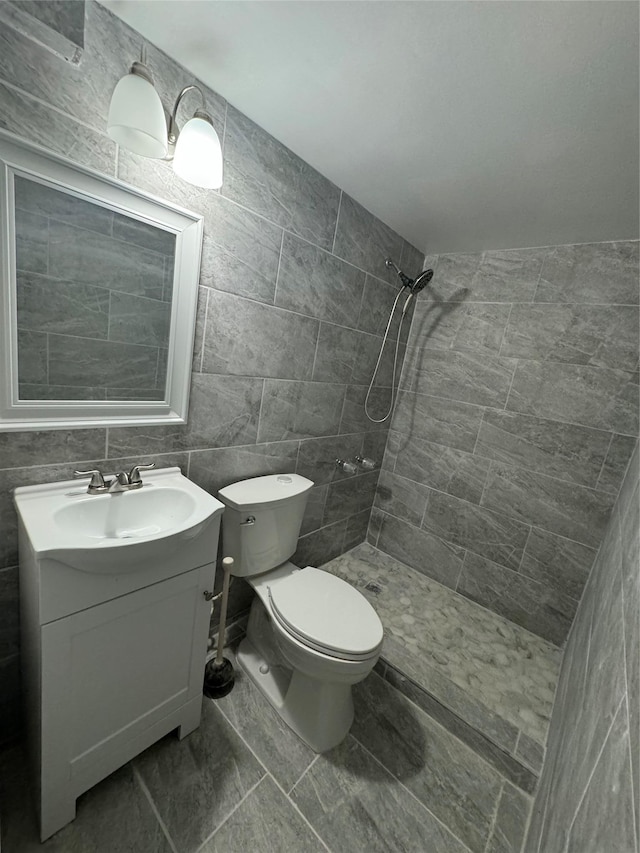 full bath featuring vanity, tile walls, toilet, and tiled shower