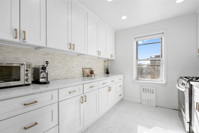 kitchen with stainless steel range with gas cooktop, white cabinets, light stone counters, and decorative backsplash