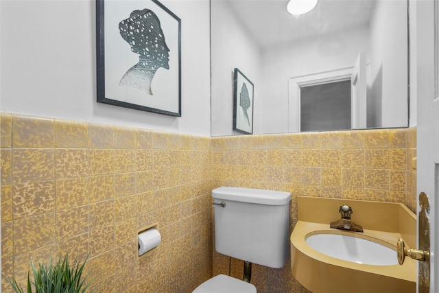 bathroom with wainscoting, a sink, toilet, and tile walls