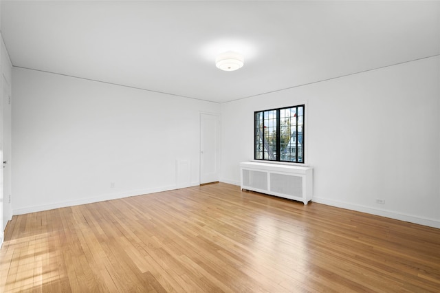 empty room featuring baseboards, light wood finished floors, and radiator heating unit