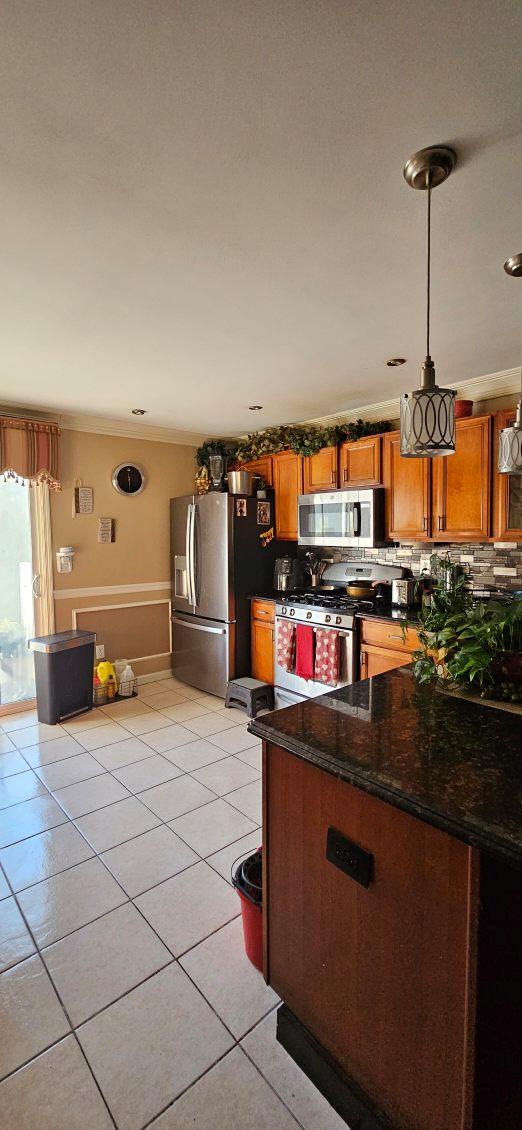 kitchen featuring pendant lighting, light tile patterned floors, crown molding, stainless steel appliances, and dark stone counters